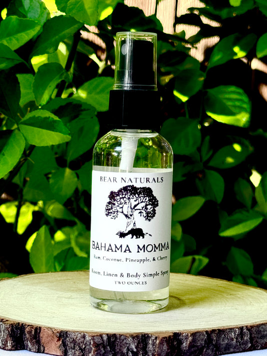 A clear bottle with a black fingertip style spray nozzle featuring a white label with black writing on a wooden surface with green leaves in the background.