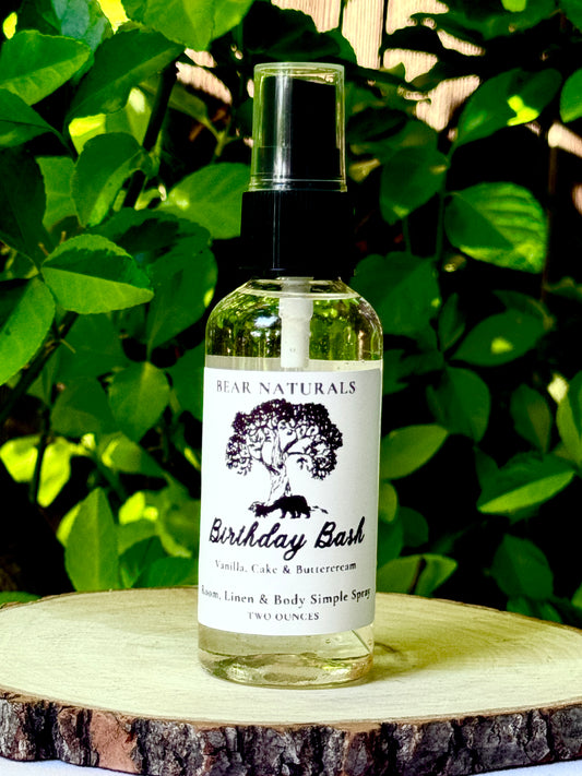 A clear bottle with a black fingertip style spray nozzle featuring a white label with black writing on a wooden surface with green leaves in the background.