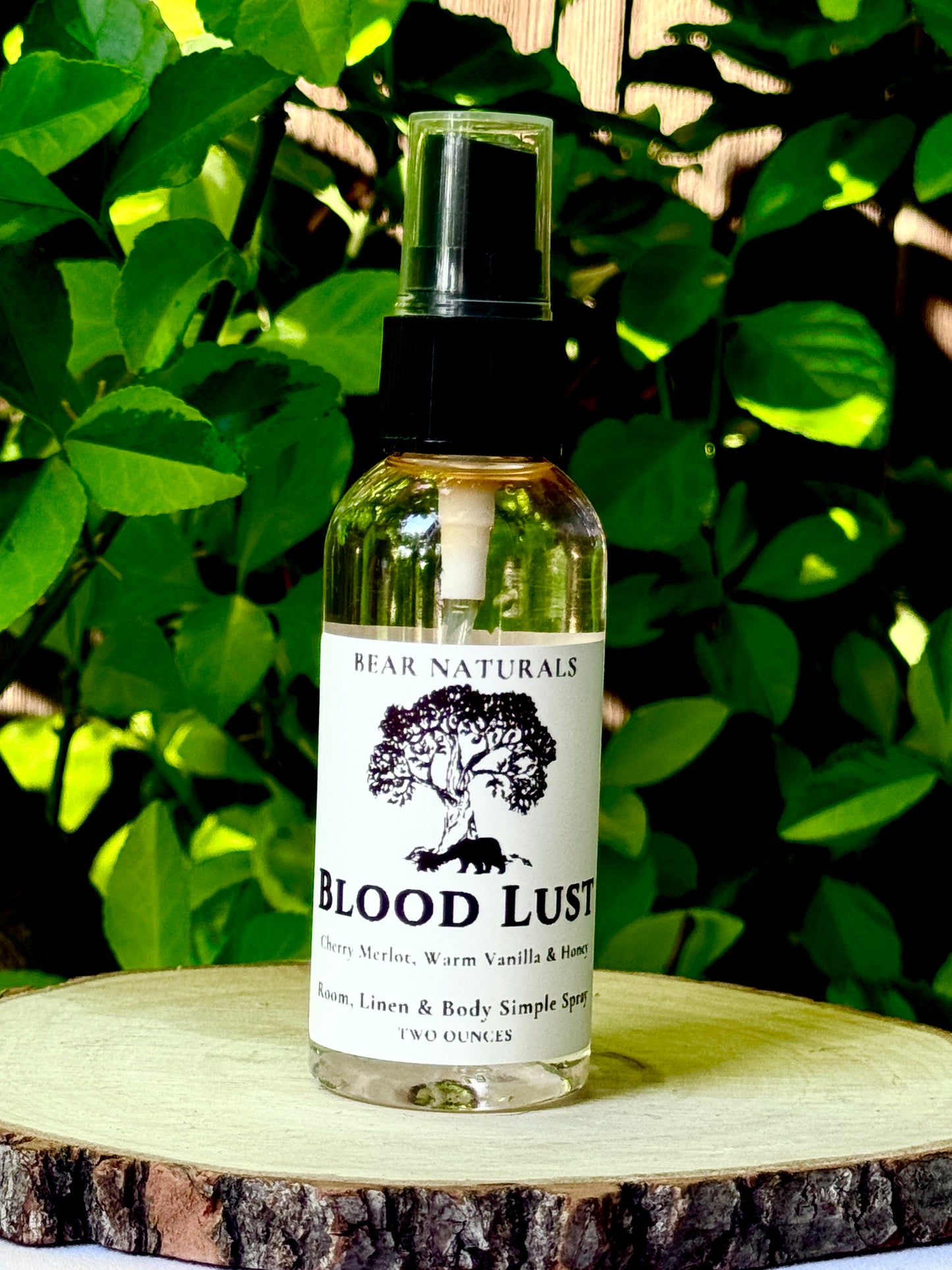 A clear bottle with a black fingertip style spray nozzle featuring a white label with black writing on a wooden surface with green leaves in the background.