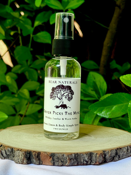 A clear bottle with a black fingertip style spray nozzle featuring a white label with black writing on a wooden surface with green leaves in the background.