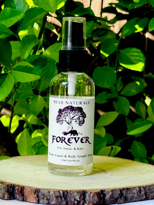 A clear bottle with a black fingertip style spray nozzle featuring a white label with black writing on a wooden surface with green leaves in the background.