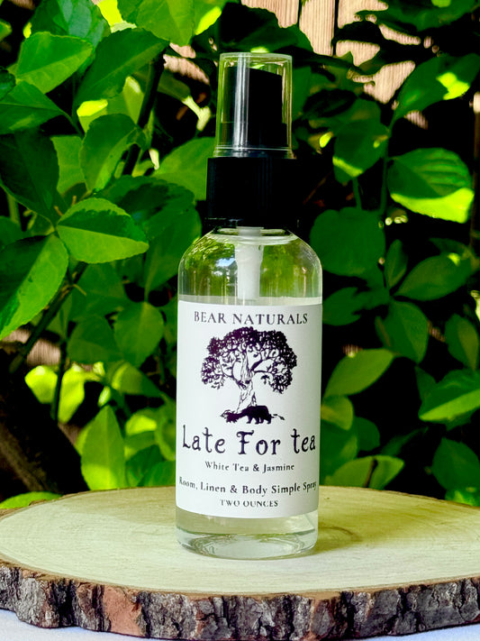 A clear bottle with a black fingertip style spray nozzle featuring a white label with black writing on a wooden surface with green leaves in the background.