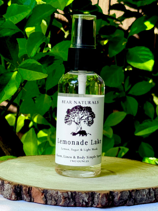 A clear bottle with a black fingertip style spray nozzle featuring a white label with black writing on a wooden surface with green leaves in the background.