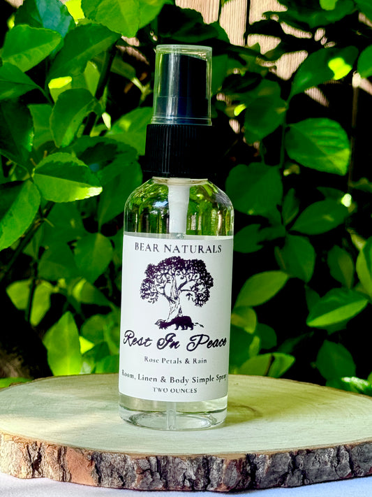 A clear bottle with a black fingertip style spray nozzle featuring a white label with black writing on a wooden surface with green leaves in the background.