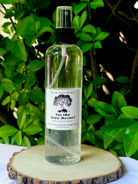 A clear bottle with a black fingertip style spray nozzle featuring a white label with black writing on a wooden surface with green leaves in the background.