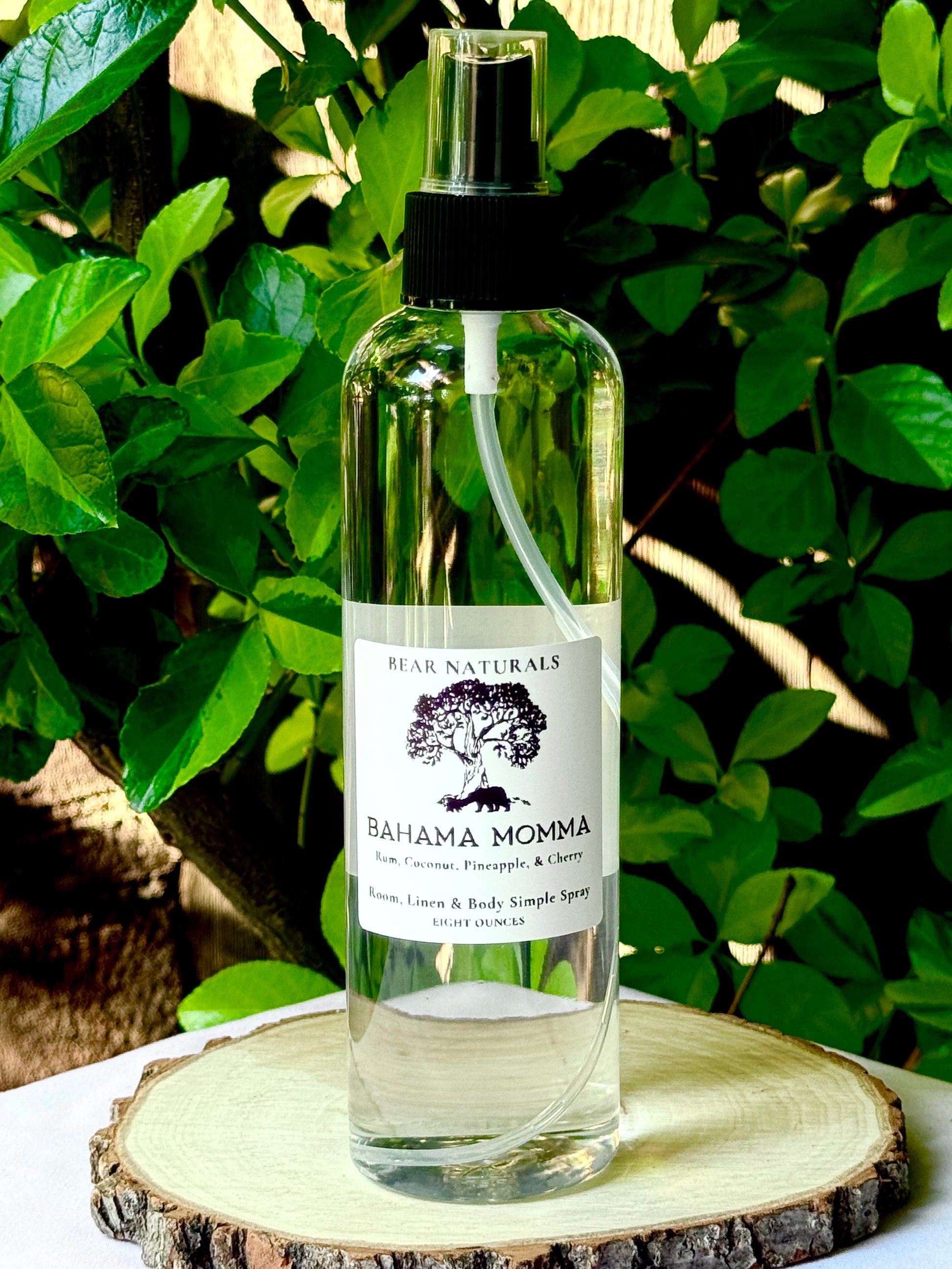 A clear bottle with a black fingertip style spray nozzle featuring a white label with black writing on a wooden surface with green leaves in the background.