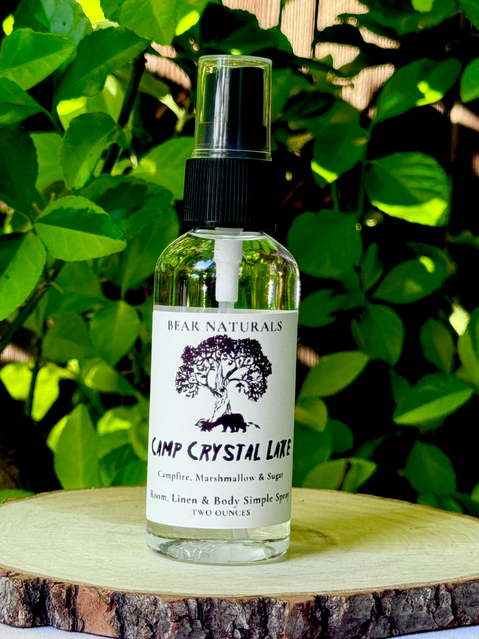 A clear bottle with a black fingertip style spray nozzle featuring a white label with black writing on a wooden surface with green leaves in the background.