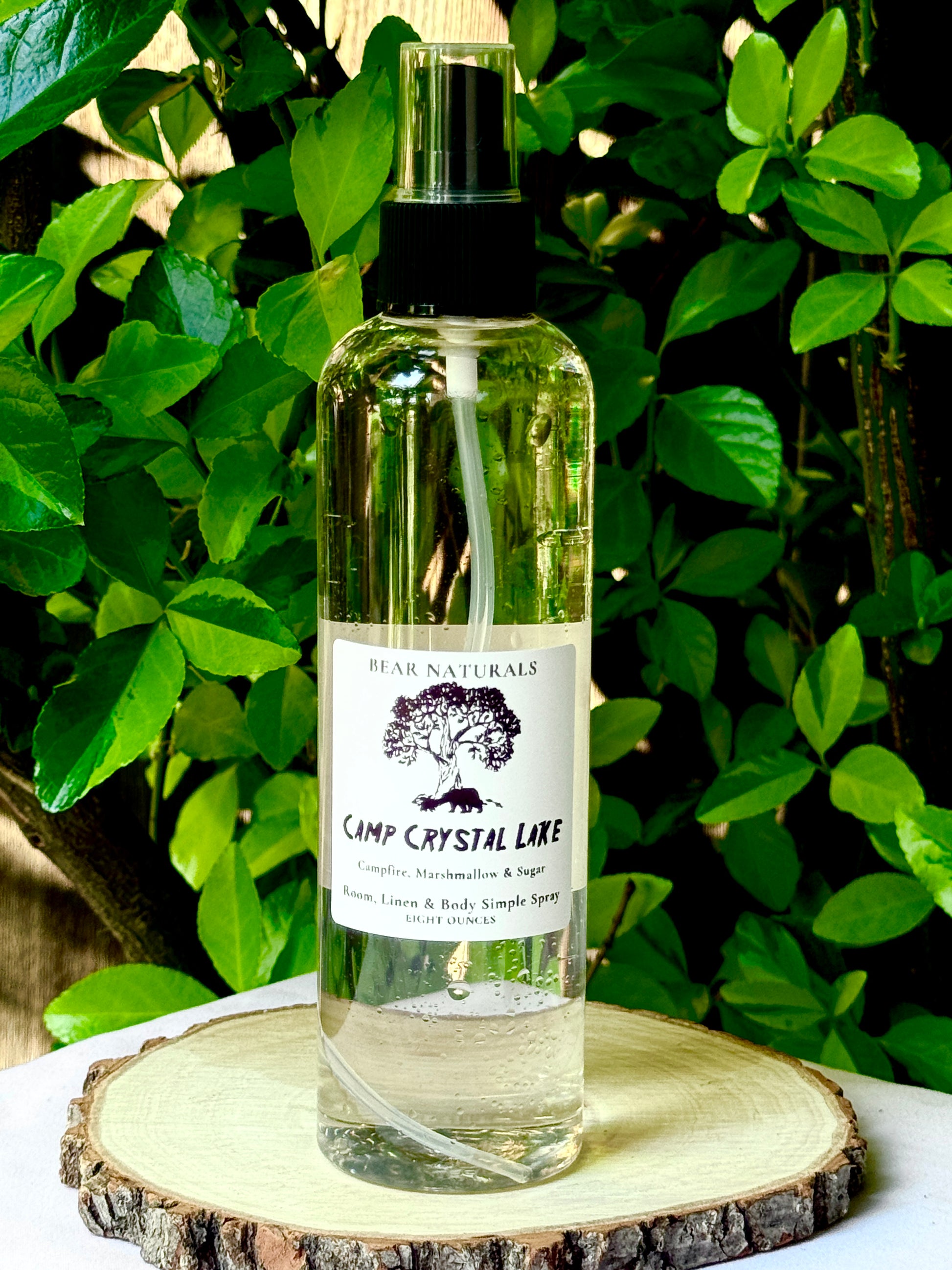 A clear bottle with a black fingertip style spray nozzle featuring a white label with black writing on a wooden surface with green leaves in the background.