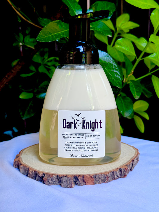 an 8 ounce bottle of 'Dark Knight' all natural beard wash on a wooden coaster with green leaves in the background