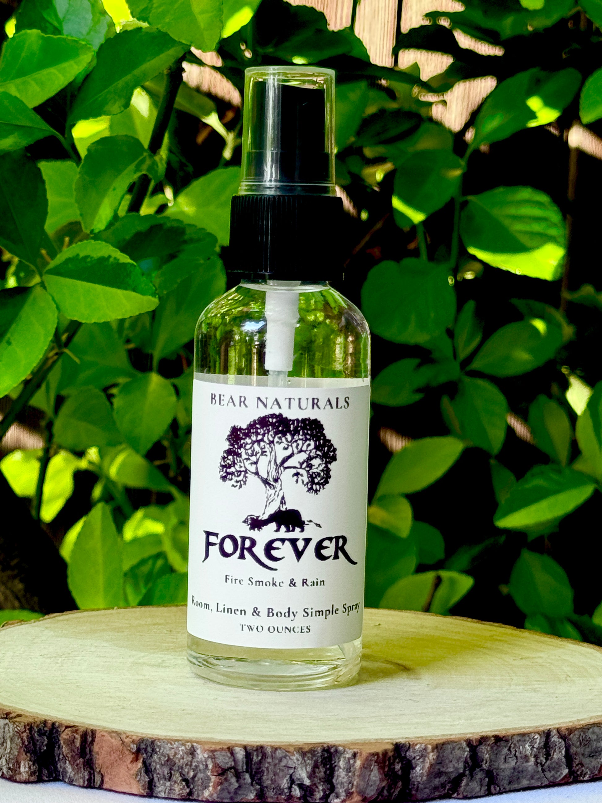 A clear bottle with a black fingertip style spray nozzle featuring a white label with black writing on a wooden surface with green leaves in the background.