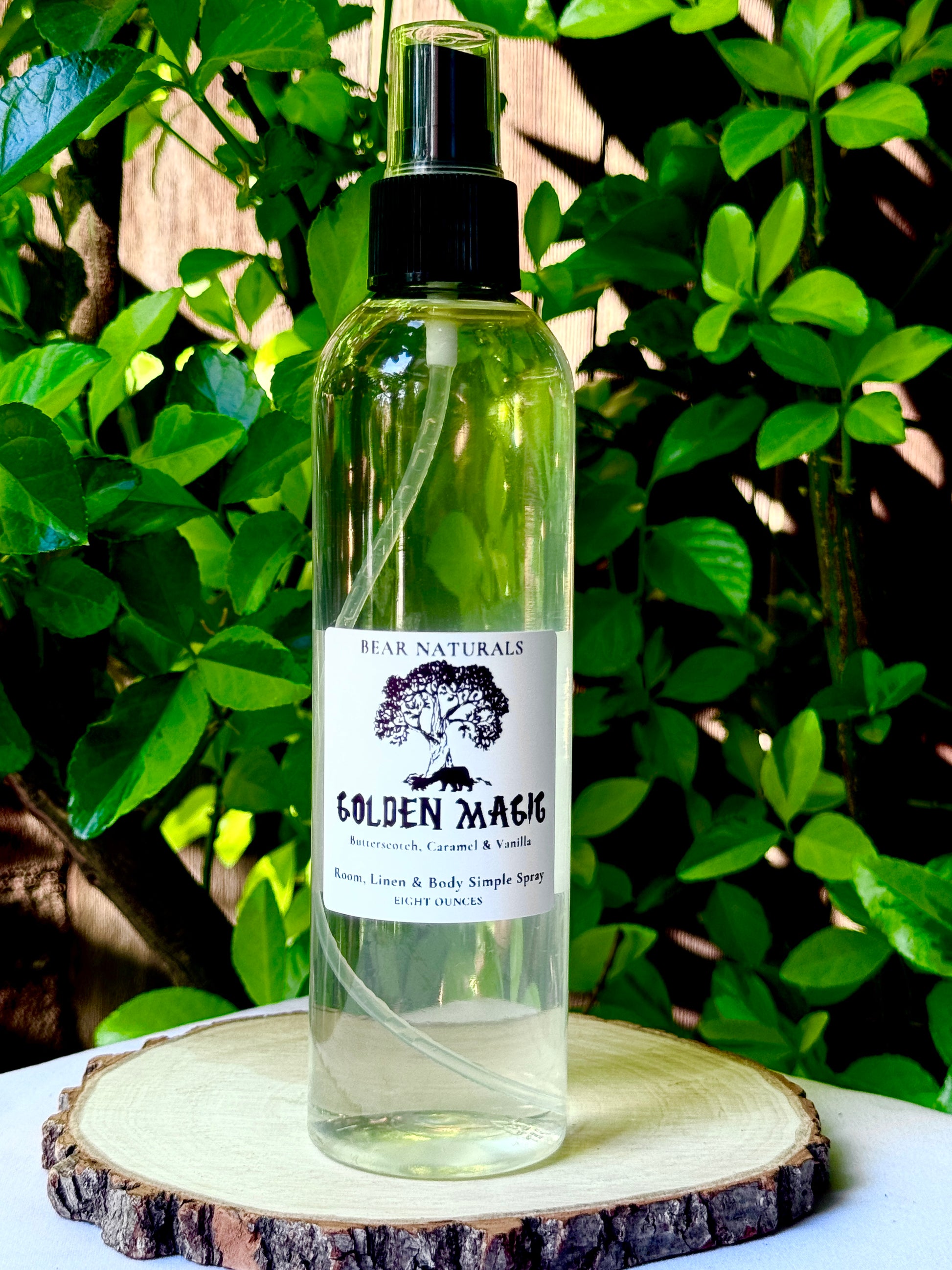 A clear bottle with a black fingertip style spray nozzle featuring a white label with black writing on a wooden surface with green leaves in the background.
