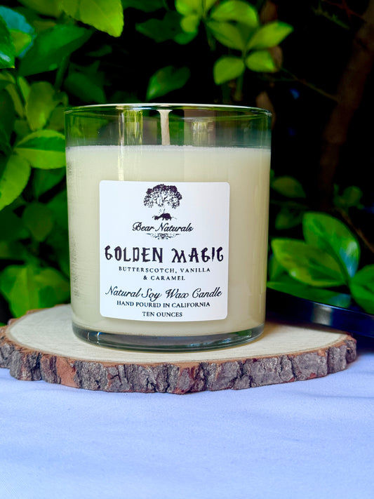 a ten ounce white candle in a clear jar featuring a white label with black writing on a wooden surface with green leaves in the back ground.