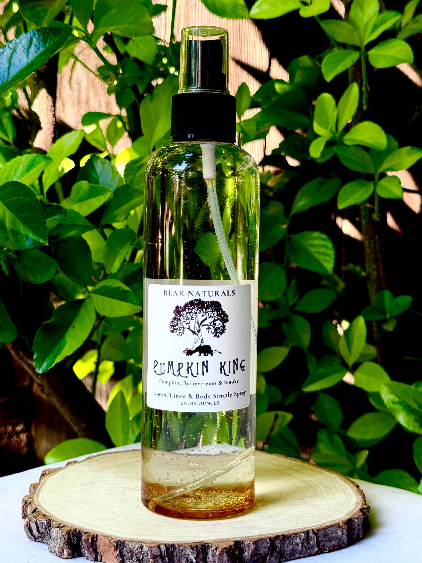 A clear bottle with a black fingertip style spray nozzle featuring a white label with black writing on a wooden surface with green leaves in the background.