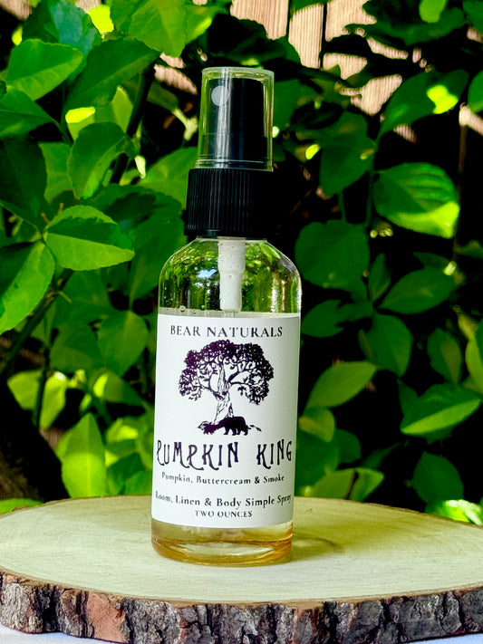 A clear bottle with a black fingertip style spray nozzle featuring a white label with black writing on a wooden surface with green leaves in the background.