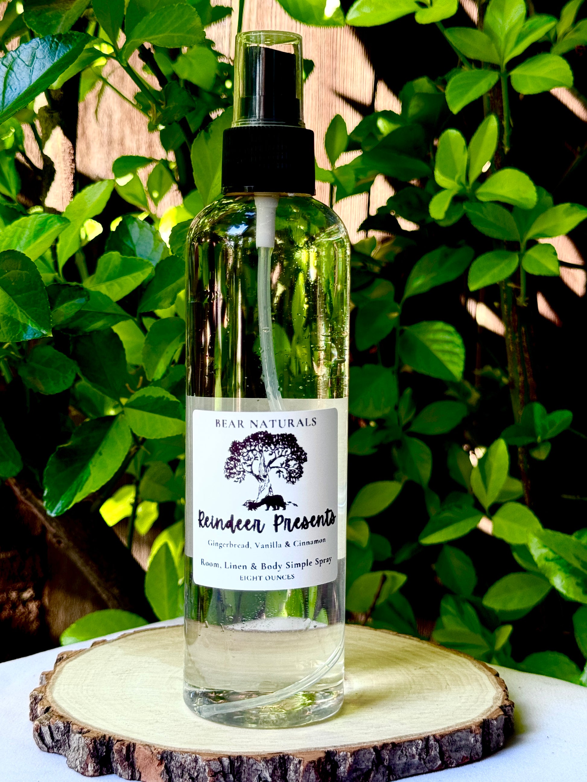 A clear bottle with a black fingertip style spray nozzle featuring a white label with black writing on a wooden surface with green leaves in the background.