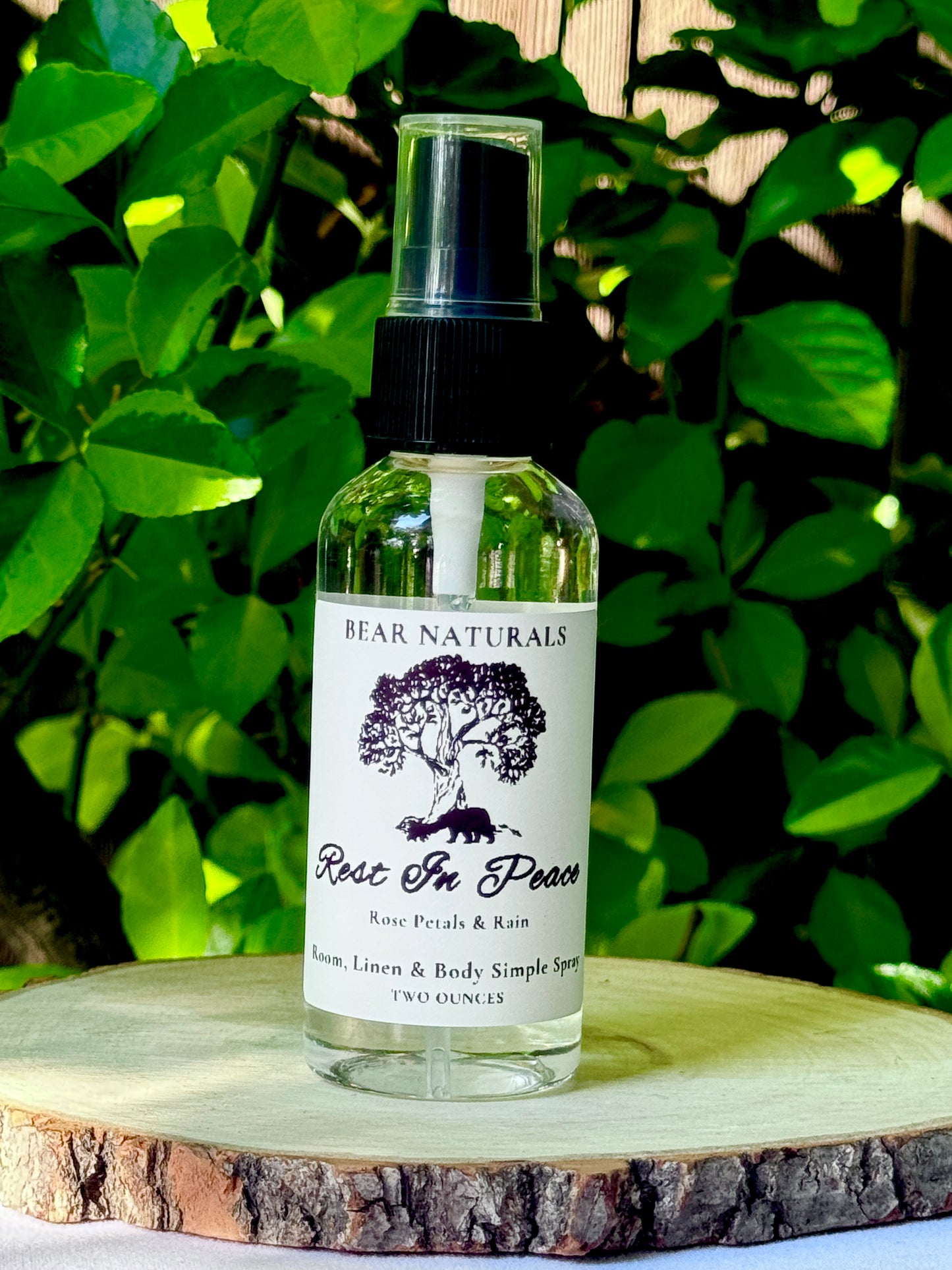 A clear bottle with a black fingertip style spray nozzle featuring a white label with black writing on a wooden surface with green leaves in the background.
