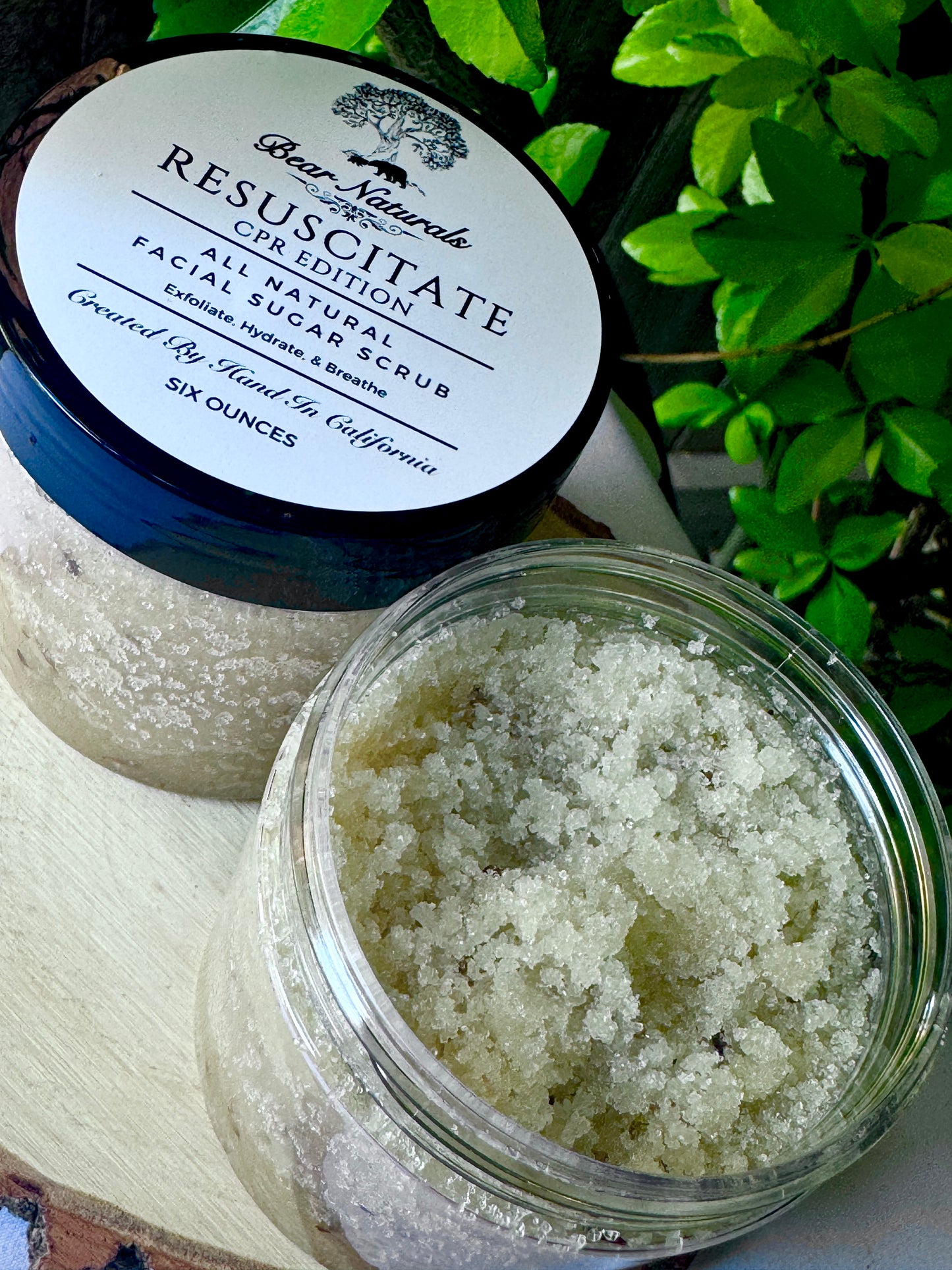 Jar of resuscitate all natural exfoliating sugar scrub CPR edition on a wooden stand with leaves in the background 