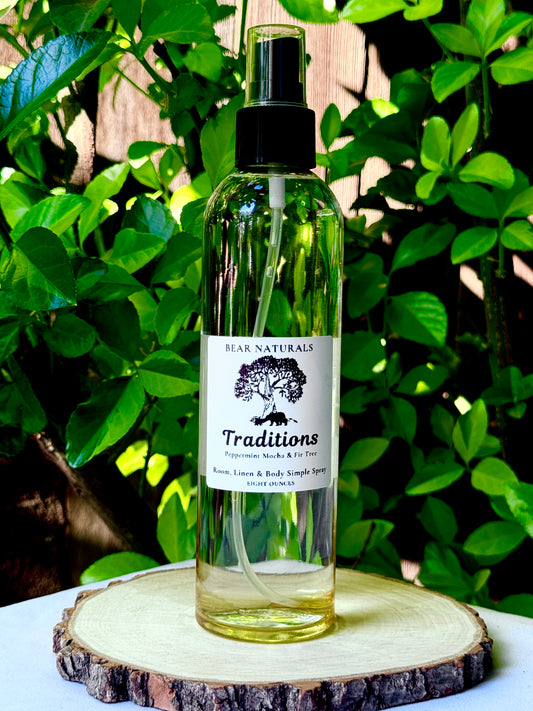 A clear bottle with a black fingertip style spray nozzle featuring a white label with black writing on a wooden surface with green leaves in the background.