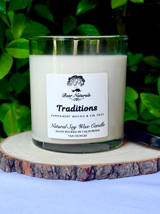 a ten ounce white candle in a clear jar featuring a white label with black writing on a wooden surface with green leaves in the background.