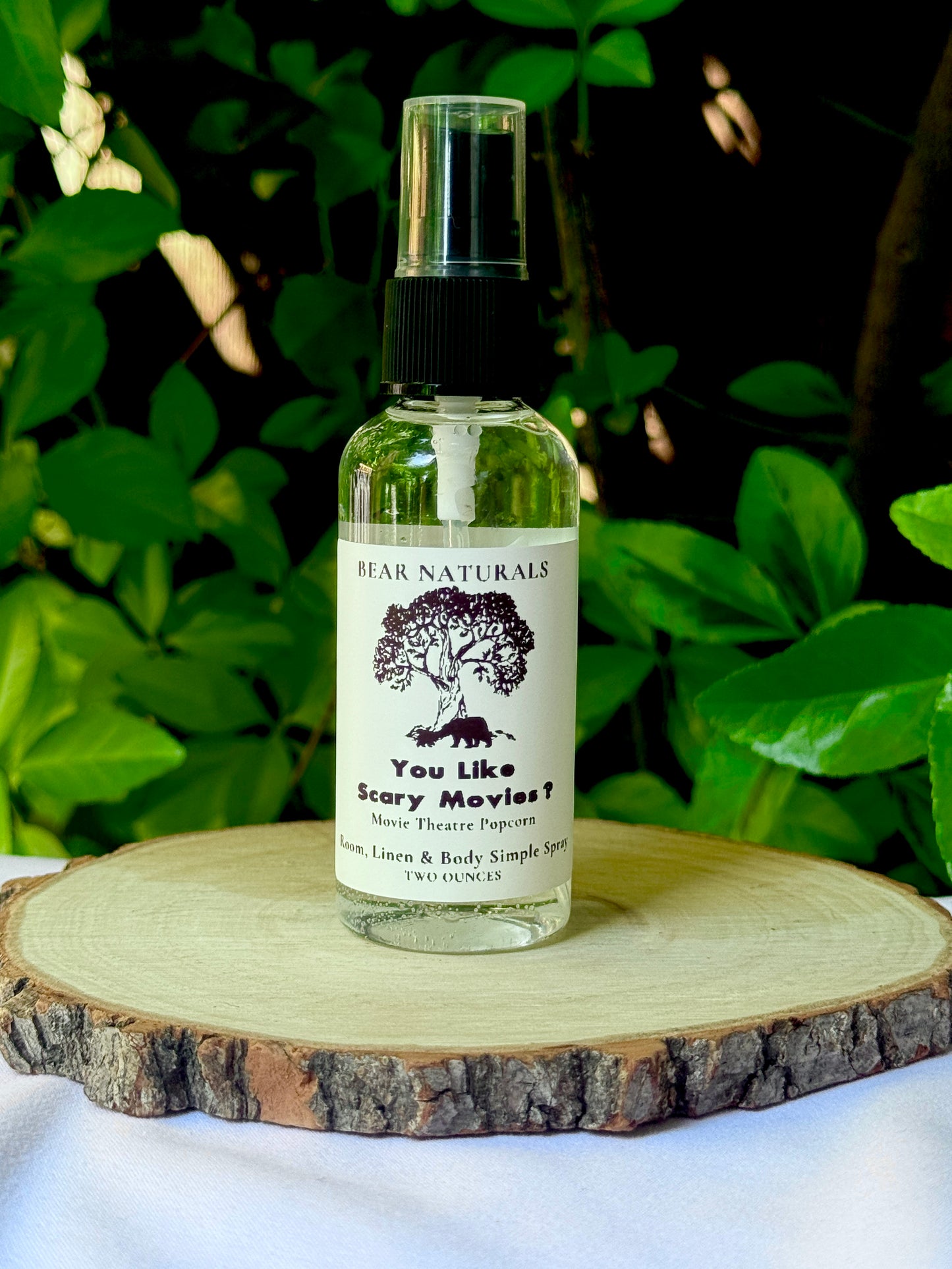 A clear bottle with a black fingertip style spray nozzle featuring a white label with black writing on a wooden surface with green leaves in the background.